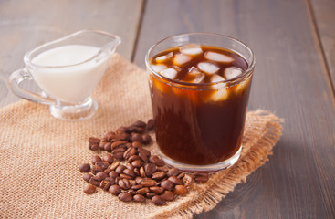 Iced latte coffee with ice cubes and coffee beans on a table.
