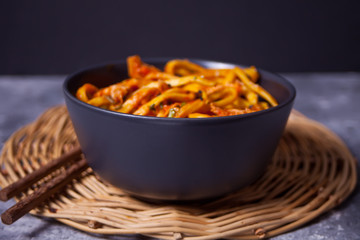 Udon noodles with chicken meat in bowl on dark stone background.