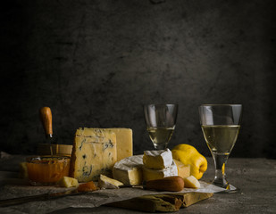 Low key still life with various cheeses, wine in glasses, quince fruit, and jam