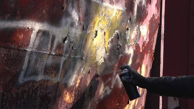 Homeless man spray painting old train wagon with aerosol can