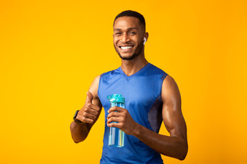 Afro sportsman holding water bottle listening to music