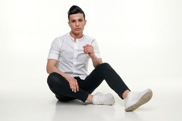 Handsome, young, trendy man is sitting on the floor in studio