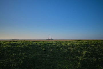 Fototapeta na wymiar Blick über den Deich mit dem Leuchtturm Westerheversand in der Ferne am Horizont