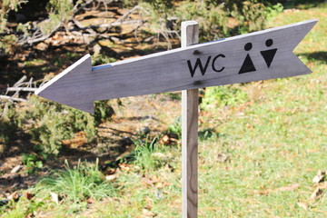 Toilet pointer in the form of a wooden arrow with special symbols drawn in black paint . wooden toilet sign gives the direction to the toilet