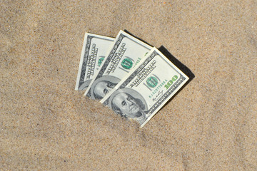 Fototapeta na wymiar Money dolars half covered with sand lie on beach close-up.