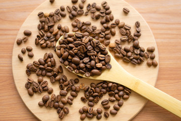 Wooden spoon with coffee grains on a light wooden round background with grains.Top view.