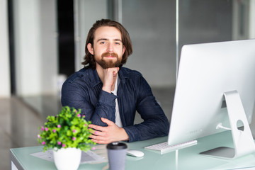 Portrait of young man working on computer sitting at his desk in the office