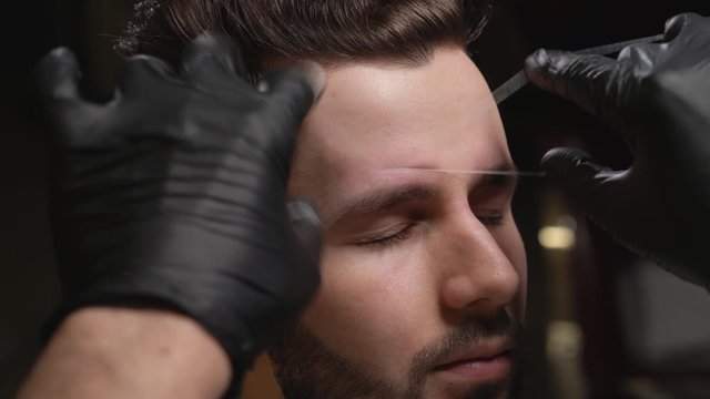 Barber in black gloves doing threading procedure for client
