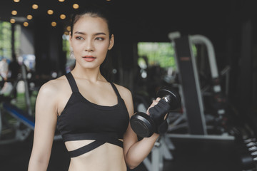 Fototapeta na wymiar muscular young asian pretty slim body woman exercise with dumbbell in fitness gym with machine in background, bodybuilder, healthy lifestyle, exercise fitness, workout and sport training concept