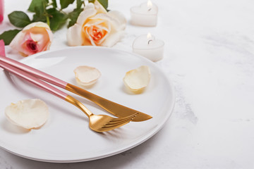 Plate with fork, knife and rose petals and roses a white table close-up.