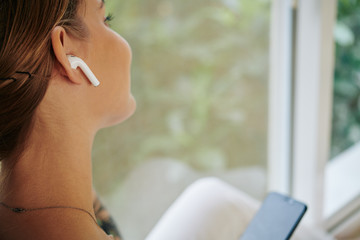 Unrecognizable young woman with modern wireless earphones enjoying music horizontal close up shot