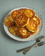 Homemade syrniki on a round light plate forks closeup