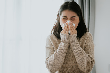 Sick Asian woman using a tissue to sneeze at home