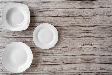 White empty ceramic plates in different shapes on old wooden background of a table. Plates clean for kitchen, porcelain dishware. Top view with copy space for text.