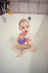 Little baby holding a toy in the bathtub with water. Cute infant toddler at bathing time.
