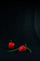 Two red sweet peppers and two green cucumbers on a black cloth background