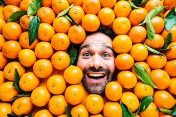 Man with ripe oranges, concept for food industry. Face of grimacing man in oranges or mandarins...