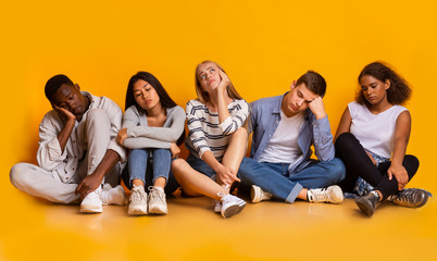 Bored classmates sitting over yellow background, being tired after classes