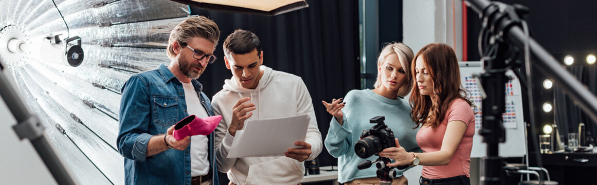 Panoramic Shot Of Art Director Holding Pink Shoe Near Coworkers In Photo Studio