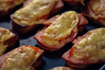 Many baked hot sandwiches with ham and cheese lie on a tray in a row.
