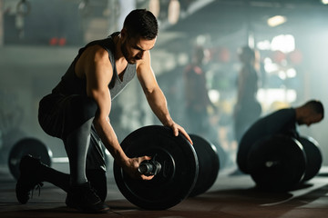 Fototapeta na wymiar Young sportsman adjusting barbell on weight training in a gym.