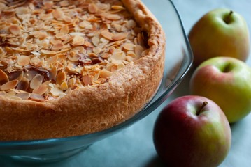Homemade apple pie with mascarpone filling covered with almond petals on a glass cake stand and...