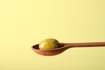 Wooden spoon with olive on beige background, close up