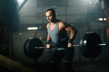 Fototapeta na wymiar Athletic man making an effort while weightlifting on strength training in a gym.