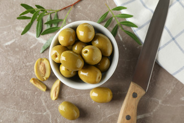 Bowl with olives, leaves, knife and towel on grey background, top view