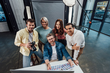 overhead view of happy creative director and assistants looking at camera in photo studio