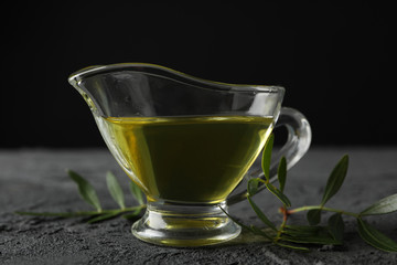 Leaves and gravy boat with olive oil on black background, close up