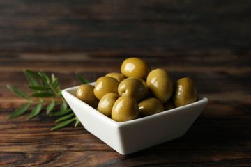 Leaves and square bowl with olives on wooden background, close up