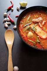 Thai food background concept. Dish of Thailand cuisine. Tom yum soup in black dish, rice in wooden plate, wooden ladle and spoon, chilis, garlic on table dark background, thai food vertical picture