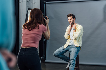 back view of photographer taking photo of handsome model posing while sitting on chair