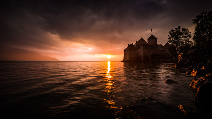 Sunset on a castle by the lake. Calm water, cloudy weather. The sun sets opposite.
