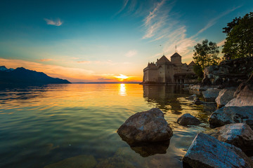 Sunset on a castle by the lake. Calm water, cloudy weather. The sun sets opposite.