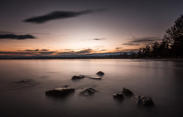 Calm water on the lake with some stones coming out. Soothing sunset