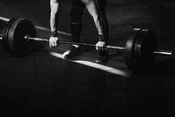 Unrecognizable sportsman exercising with barbell in a gym.