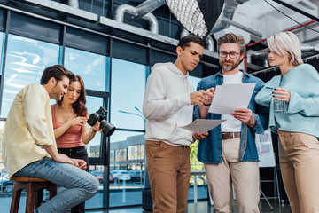 creative director in glasses looking at photo near coworkers