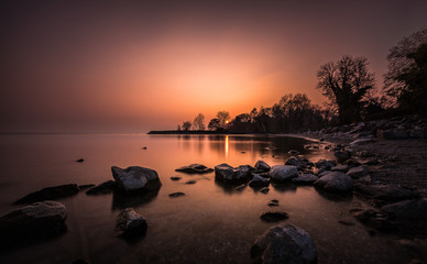 Sunset in fire on a calm and silent lake. Silence like stones in the foreground
