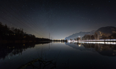 Night landscape by a lake, reflection of the sky in the lake, lights of vehicle headlights on the highway