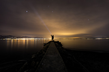 lonely man in perspective, at night, facing the lake, reflections, flashlight, isolated