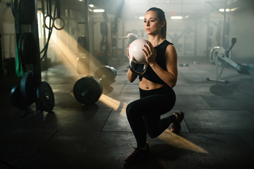 Athletic woman doing split squats while exercising with kettle bell in a gym.