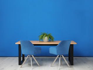 Modern table with potted fern near blue wall