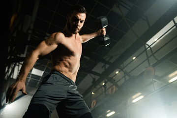 Fototapeta na wymiar Below view of dedicated sportsman exercising with dumbbell in a gym.