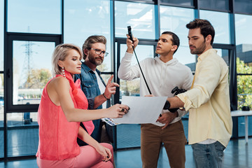 attractive model and bearded art director looking at photo collage with assistants