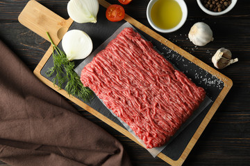 Spices and cutting board with minced meat on wooden background, top view