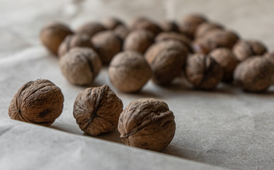 Side view. Three inshell walnuts opposite a handful of nuts. on old crumpled kraft paper, brown background, warm beige