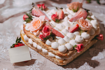 White cream sponge cake in the shape of a heart with roses and strawberries. Template for a note.  Close-up
