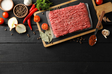 Spices and cutting board with minced meat on wooden background, top view